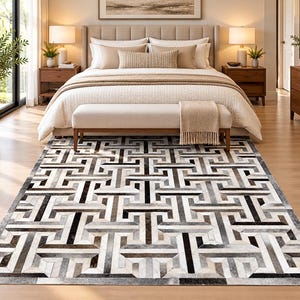 May include: A rectangular area rug featuring a geometric Greek key pattern composed of stitched leather patches in shades of black, white, gray, and brown, creating a high-contrast, textured surface that covers the floor space.