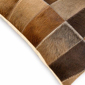 May include: A square throw pillow constructed from a patchwork of rectangular hide panels in varying shades of brown, tan, and dark chocolate. The individual pieces are joined together with visible white stitching along the seams.