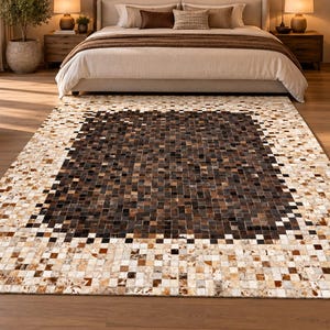 Puede incluir: Una alfombra rectangular con un patrón de mosaico compuesto por pequeñas piezas cuadradas. El centro consta de tonos marrón oscuro y negro, mientras que el borde ancho muestra un degradado de tonos crema, beige, tostado y marrón claro.