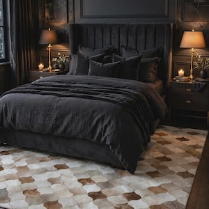 Puede incluir: Un dormitorio con una cama tapizada en gris oscuro con un cabecero alto de canales verticales, cubierta con ropa de cama y almohadas oscuras a juego, situada sobre una alfombra grande con un patrón repetitivo de formas festoneadas en marrón, beige y blanco.
