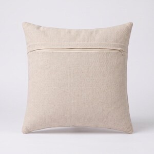 May include: A square throw pillow cover in a solid light beige color. The cover features a horizontal zipper closure positioned across the upper portion of the back side, with a visible metal zipper pull tab on the right side of the fabric.