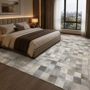 Könnte beinhalten: Ein rechteckiger Teppich mit einem Patchwork-Design aus quadratischen Fliesen in verschiedenen Grau-, Weiß- und Beigetönen. Der Teppich hat eine strukturierte Oberfläche mit sichtbaren Nähten zwischen den einzelnen Quadraten, die ein Gittermuster bilden.