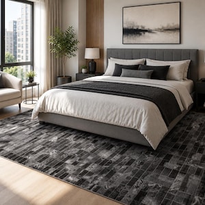 Könnte beinhalten: Ein rechteckiger Teppich mit einem dunkelgrauen und schwarzen Mosaikfliesenmuster in Used-Optik. Der Teppich liegt auf einem hellen Holzboden unter einem Bett mit grauem Polsterkopfteil, weißer Bettwäsche und dunkelgrauen Dekokissen.
