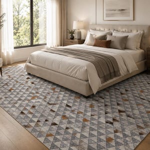 May include: A large area rug featuring a repeating geometric pattern of triangles in shades of grey, white, and brown. The rug covers the floor beneath a bed, showcasing a textured surface with a consistent triangular grid design throughout.