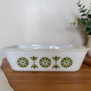 May include: A rectangular white glass baking dish featuring a repeating pattern of green starburst and diamond-shaped motifs along the exterior side. The dish has a smooth, glossy finish with a wide rim and slightly tapered sides.