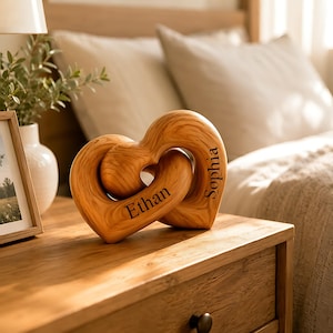 May include: A light brown wooden sculpture featuring two interlocking heart shapes. The surface displays a natural wood grain pattern. The name Ethan is engraved on the left heart, and the name Sophia is engraved on the right heart in black.