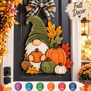 May include: A wooden door hanger featuring a gnome with a green hat and white beard, holding a small orange pumpkin. The gnome is surrounded by orange, green, and white pumpkins and autumn leaves, topped with a black and white buffalo plaid bow.