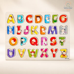 May include: A rectangular wooden alphabet puzzle board featuring twenty-six colorful letter-shaped pieces, each with a small white wooden knob for grasping. Every letter corresponds to an illustration and a word, from A for apple to Z for zebra.
