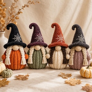 Pode incluir: Quatro figuras de gnomos em crochê com chapéus pontiagudos com teias de aranha bordadas. Os gnomos têm tranças de fio e corpos em forma de abóbora nas cores laranja, verde, creme e malva. Cada chapéu é finalizado com uma ponta curva.