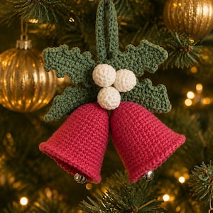 May include: A crochet Christmas ornament featuring two red bells hanging below three white spheres and two green holly leaves. The ornament includes a green loop at the top for hanging and small silver jingle bells inside each red crochet bell.