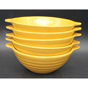 May include: A stack of five bright yellow ceramic bowls, each featuring a rounded shape with horizontal ribbed detailing along the exterior and two small, protruding handles on opposite sides for easy gripping and handling.