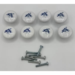 May include: Eight round white ceramic cabinet knobs featuring a blue floral pattern painted on the surface. The set includes eight matching silver-colored metal screws for installation, arranged in a pile below the knobs.