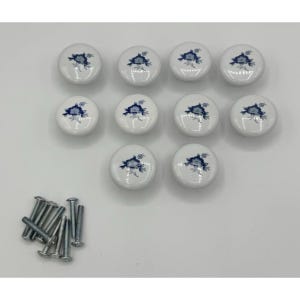 May include: A set of ten round white ceramic cabinet knobs, each featuring a blue floral pattern. The knobs are arranged in rows and are accompanied by ten silver-colored metal screws for installation, shown in the bottom left corner.