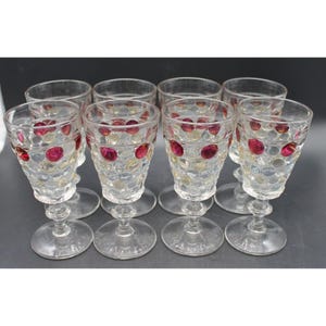May include: A set of eight clear glass goblets featuring a textured hobnail pattern. Each glass is decorated with alternating raised dots in vibrant red and translucent gold, supported by a clear glass stem and a circular base for stability.