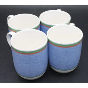 Op de afbeelding: Een set van vier keramische mokken met een gespikkeld blauw lichaam en een witte binnenkant. Elke mok is versierd met een horizontale band nabij de bovenrand, bestaande uit een dunne oranje streep en een bredere groene streep.