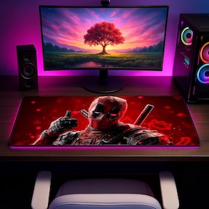May include: A rectangular desk mat featuring a graphic print of the character Deadpool in a red and black suit, giving a thumbs-up gesture against a dark red background with glowing red bokeh light effects and two katana handles visible.