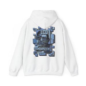May include: A white hooded sweatshirt featuring a graphic on the back with the text LCD SOUNDSYSTEM, SASQUATCH! MUSIC FESTIVAL, and THE GORGE. The design consists of a fragmented portrait in shades of blue and grey, surrounded by 3D blocks.