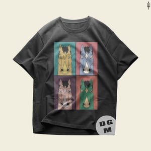 Könnte beinhalten: Ein anthrazitfarbenes Kurzarm-T-Shirt mit einer zentralen Grafik von vier Pferdeköpfen in einem Raster. Jedes Pferd ist in einer anderen Farbe dargestellt—beige, blau, hellviolett und grün—vor kontrastierenden Hintergründen. Ein kreisförmiges Logo mit den Buchstaben DG M ist in der unteren rechten Ecke sichtbar.