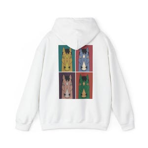 Könnte beinhalten: Ein weißer Kapuzenpullover mit einem Grafikdruck auf der Rückseite. Der Druck besteht aus vier rechteckigen Feldern, die jeweils einen stilisierten Pferdekopf in einer anderen Farbe zeigen: gelb, blau, hellrosa und grün, alle mit schwarzer Mähne.