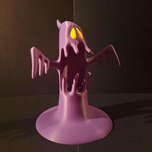 May include: A purple 3D printed ghost figurine with a wide, circular base. The ghost has a hollow, open-mouthed expression with two bright yellow, almond-shaped eyes. Its arms are outstretched to the sides, and the body features a smooth, layered texture.