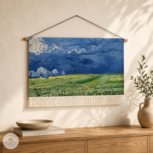 May include: A rectangular wall hanging featuring a printed landscape painting of a green field under a dark blue, cloudy sky. The textile piece is suspended from a thin black cord attached to a wooden rod and finished with a white fringe at the bottom.