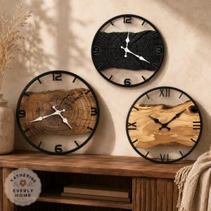 May include: Three circular wall clocks featuring natural wood slices set within black metal frames. Two clocks display Arabic numerals, while one features Roman numerals. Each clock has white or black hands centred on the wood grain patterns.