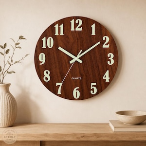 May include: A round wall clock with a dark brown wood grain finish, featuring large, pale green luminous Arabic numerals from 1 to 12. The clock has matching pale green hour, minute, and second hands, with the word QUARTZ printed in white.