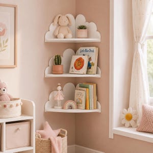 Puede incluir: Tres estantes de esquina blancos con un diseño de panel trasero en forma de nube. El estante superior sostiene un conejo de peluche y una pequeña suculenta en maceta. El estante central muestra un cactus y dos libros infantiles.
