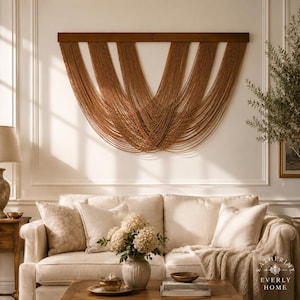 May include: A large wall hanging featuring multiple strands of brown cord suspended from a horizontal wooden bar, arranged in a series of overlapping, curved, U-shaped drapes that create a symmetrical, layered pattern across the wall surface.