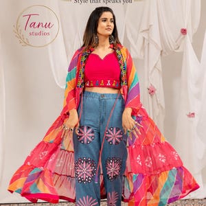 Può includere: Un top corto rosa acceso, jeans blu con ricami floreali rosa e una giacca lunga e fluida a righe multicolori. Il testo Tanu studios e Style that speaks you è visibile nella parte superiore dell'immagine.