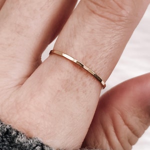 May include: A thin, polished gold ring with a flat, faceted surface band. The ring features a simple, slender design that encircles the finger, showcasing a reflective metallic finish and a consistent, narrow width throughout the entire band.