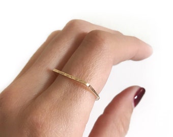 May include: A gold hammered ring with a simple, geometric design. The ring is worn on the index finger of a hand.