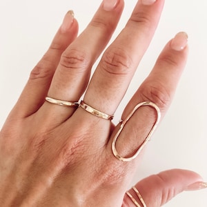 May include: A hand wearing a set of gold rings, including a large oval ring with a hammered texture.