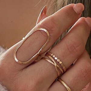 May include: A hand wearing a set of gold rings, including a large oval ring with a unique design.