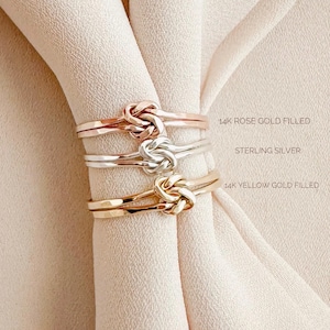 May include: Three gold rings with a knot design. The top ring is 14k rose gold filled, the middle ring is sterling silver, and the bottom ring is 14k yellow gold filled.