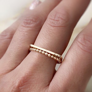 May include: A gold ring set with a thin, flat band and a delicate beaded band.