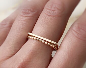 May include: A gold ring set with a thin, flat band and a delicate beaded band.