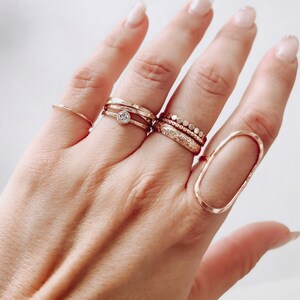 May include: A hand wearing a set of gold rings, including a ring with a small clear stone, a ring with a textured band, and a ring with a beaded band.