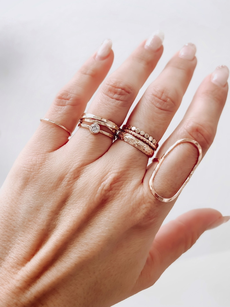 May include: A hand wearing a set of gold rings, including a ring with a small clear stone, a ring with a textured band, and a ring with a beaded band.
