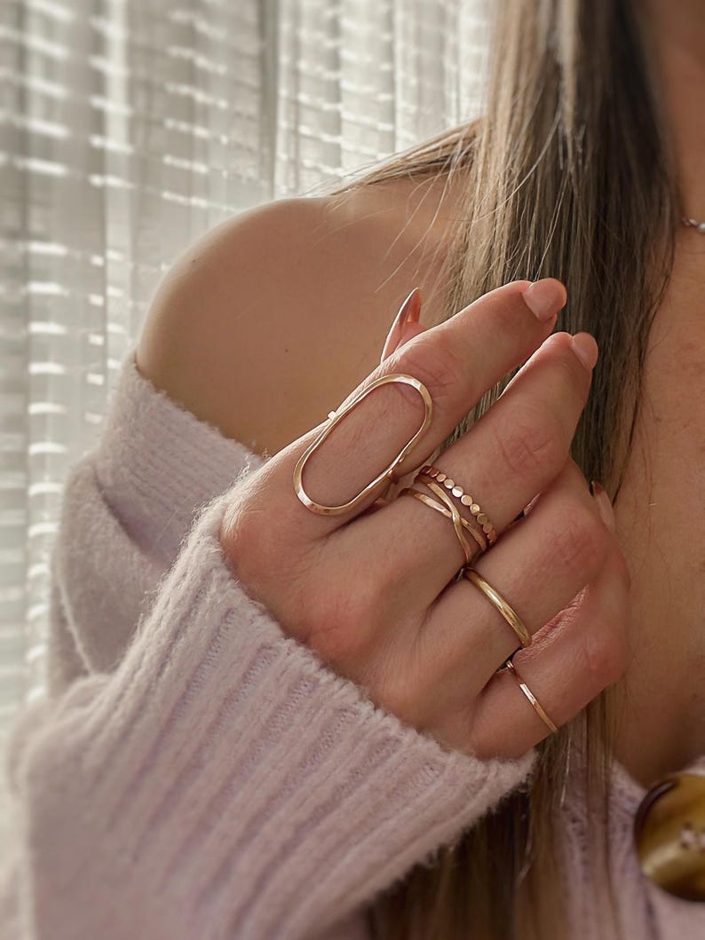 May include: A hand wearing a set of gold rings, including a large oval ring with a unique design.