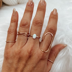 May include: A hand wearing several gold rings, including a ring with an oval-shaped opal stone. The nails are painted with a sparkly gold polish.