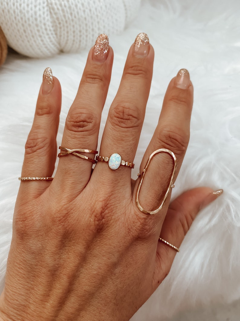 May include: A hand wearing several gold rings, including a ring with an oval-shaped opal stone. The nails are painted with a sparkly gold polish.