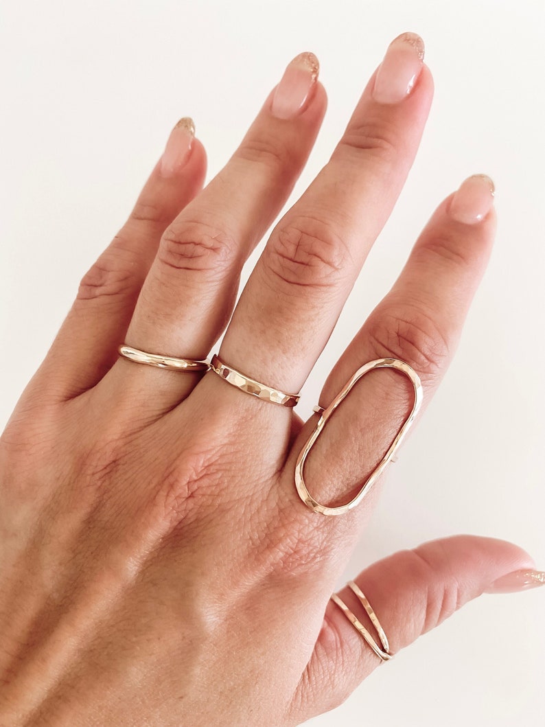 May include: A hand wearing a set of gold rings, including a large oval ring with a hammered texture.