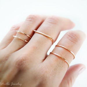May include: Four gold-toned rings stacked on a finger. The rings are thin and delicate, with a hammered texture.