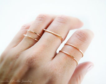Puede incluir: Cuatro anillos dorados apilados en un dedo. Los anillos son finos y delicados, con una textura martillada.