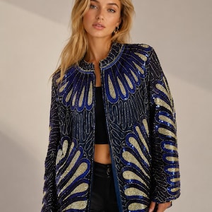 Könnte beinhalten: Eine langärmelige Jacke mit dunkelblauer Basis, verziert mit komplexen, sich wiederholenden fächerförmigen Mustern aus metallisch goldenen und leuchtend blauen Pailletten. Das Kleidungsstück hat einen hohen, runden Kragen und einen durchgehenden Reißverschluss.