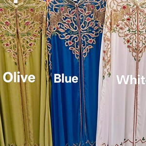 Pode incluir: Três caftãs longos abertos na frente nas cores oliva, azul e branco. Cada peça apresenta bordados complexos em dourado, rosa e verde no peito e nos ombros. O texto Olive, Blue e White está impresso sobre cada respectiva peça de roupa.