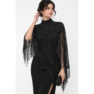 May include: A black high-neck cape top featuring intricate beadwork and embroidery across the chest and shoulders, with long beaded fringe detailing along the hem and sleeves, paired with a matching black skirt with a side slit.