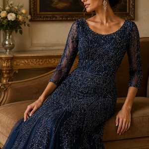 May include: A floor-length navy blue gown featuring three-quarter length sleeves and a scoop neckline. The dress is adorned with intricate tonal beadwork and sequin embroidery in a floral pattern that covers the bodice and sleeves.