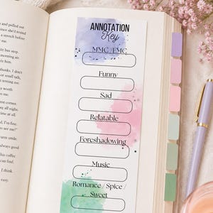 May include: A rectangular paper bookmark featuring an Annotation Key with watercolor splashes in blue, pink, and green. It lists categories including MMC/FMC, Funny, Sad, Relatable, Foreshadowing, Music, and Romance/Spice/Sweet, each with a blank space for notes.